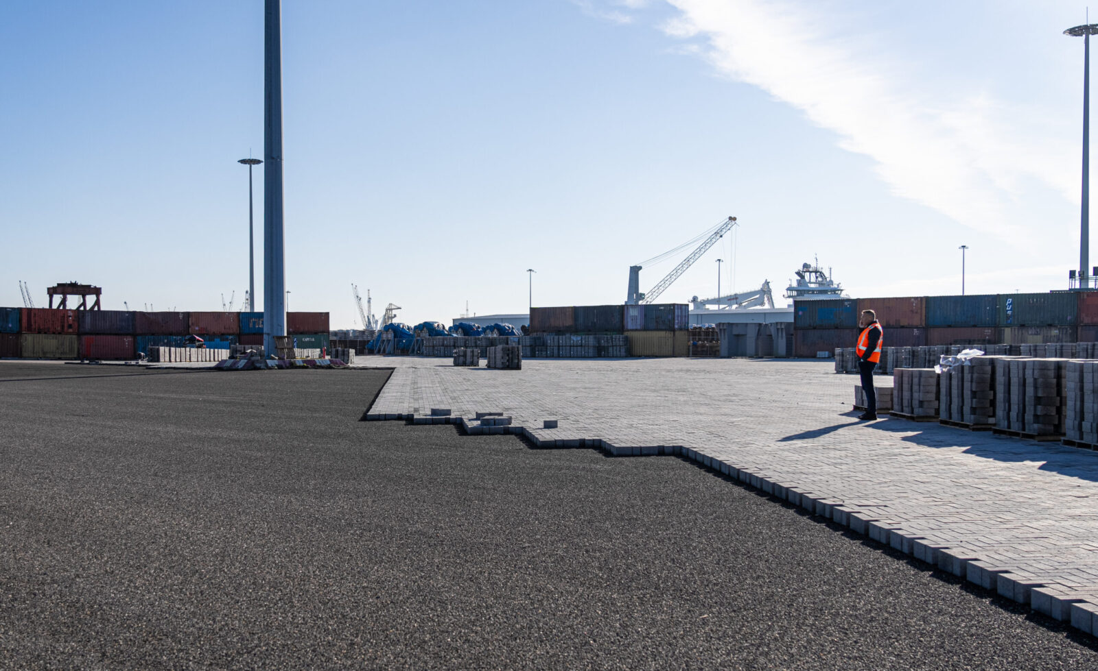 Medewerker op een groot bestraat bedrijventerrein met stapels bestratingsmateriaal op de achtergrond.