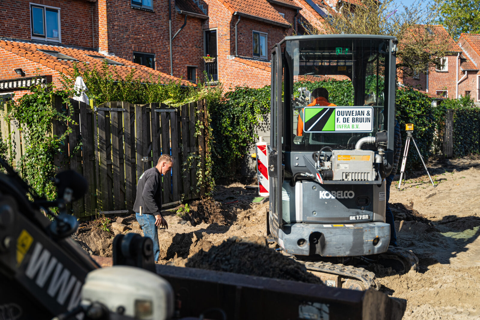 Graafmachine en medewerkers voeren grondwerk uit ter voorbereiding op nieuwe bestrating.